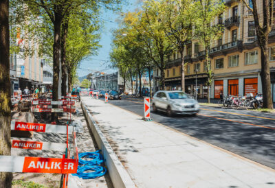 Neue, eingebaute Betonplatten für eine Busspur im innerstädtischen Strassenraum bei Tageslicht und vorbeifahrendem Verkehr.